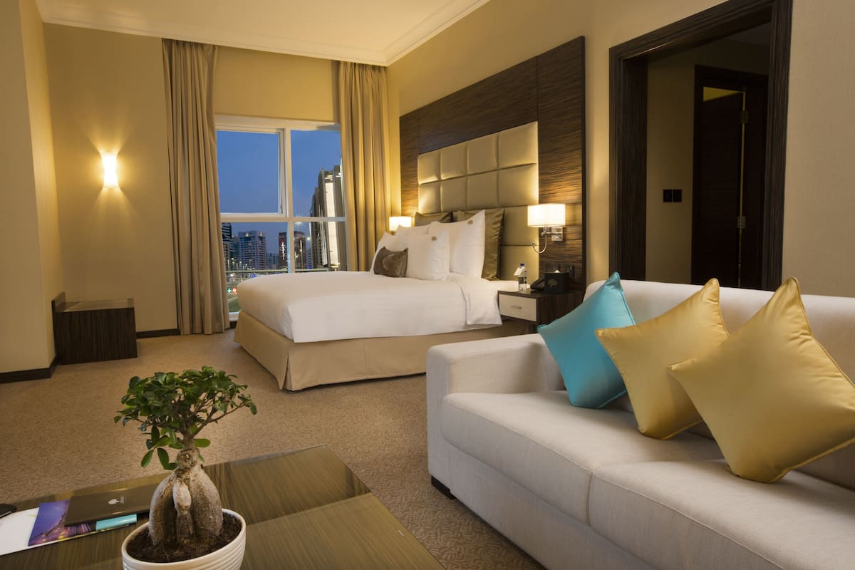 A hotel room with a bed, a sofa, a potted plant, and a view of the city.