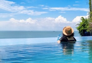 A person in a clear blue infinity pool with a view of the ocean and distant boats. - SV Boutique Resort (Ho Chi Minh City)
