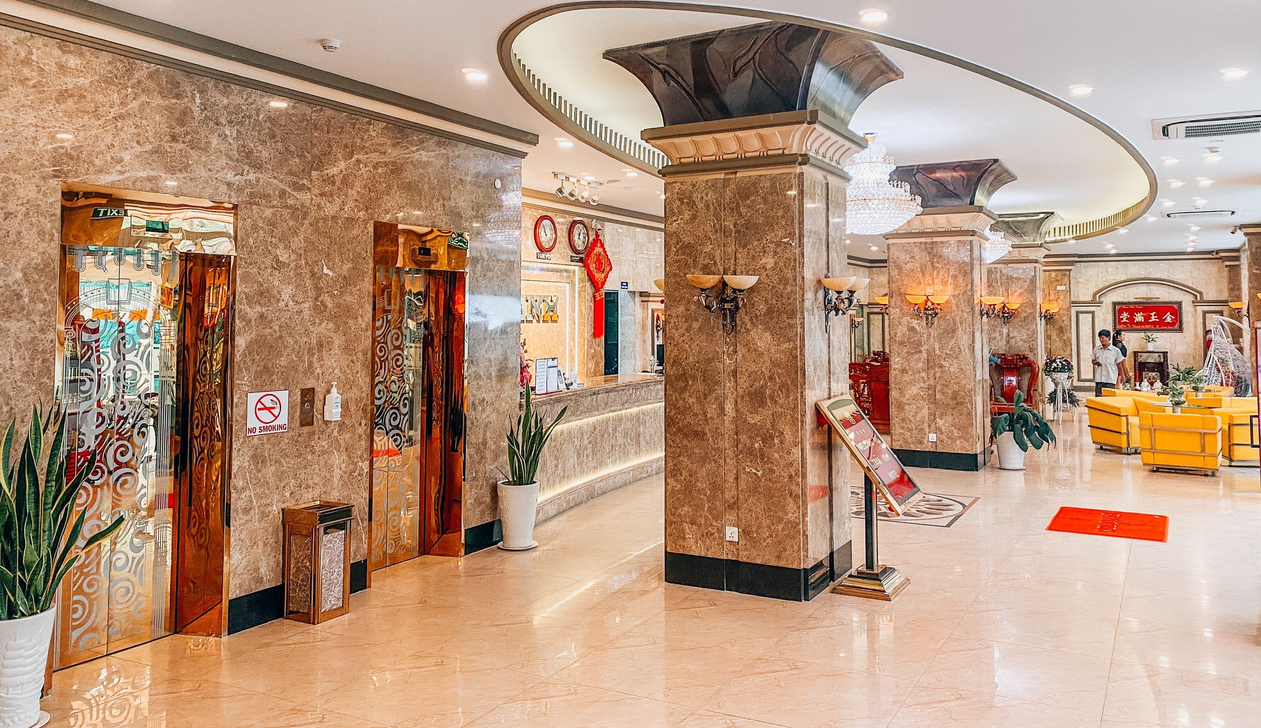 A hotel lobby with marble flooring, a reception desk, and a no-smoking sign.