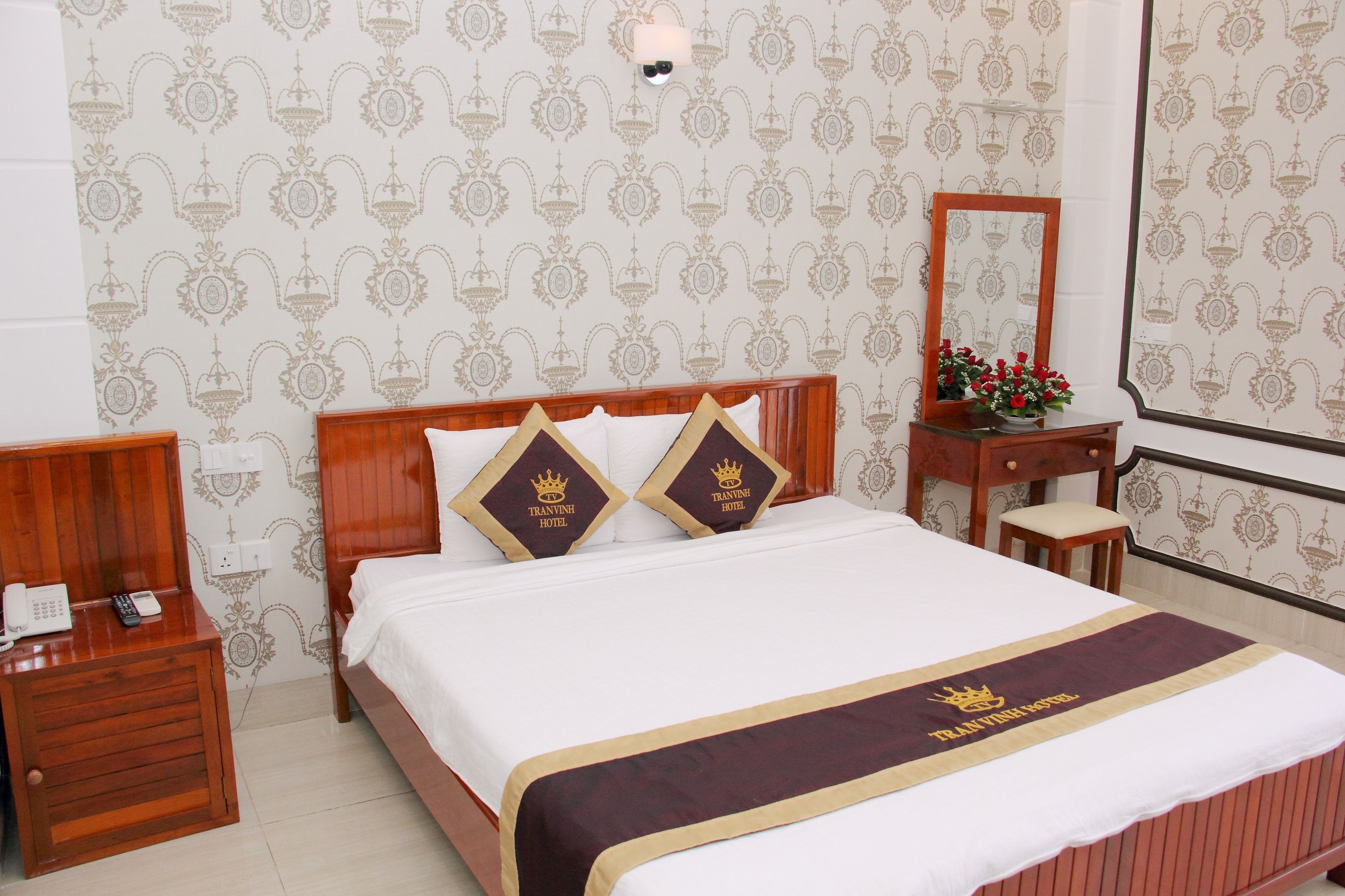 Ein Hotelzimmer mit Bett, Nachttisch, Spiegel und einem kleinen Tisch mit Blumen.