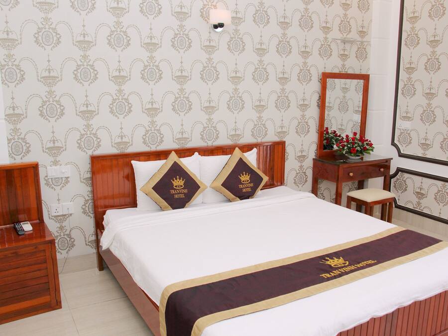 Ein Hotelzimmer mit Bett, Nachttisch, Spiegel und einem kleinen Tisch mit Blumen.