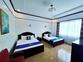 Habitación de hotel con dos camas, suelo de madera, lámpara de techo y ventana con cortinas.