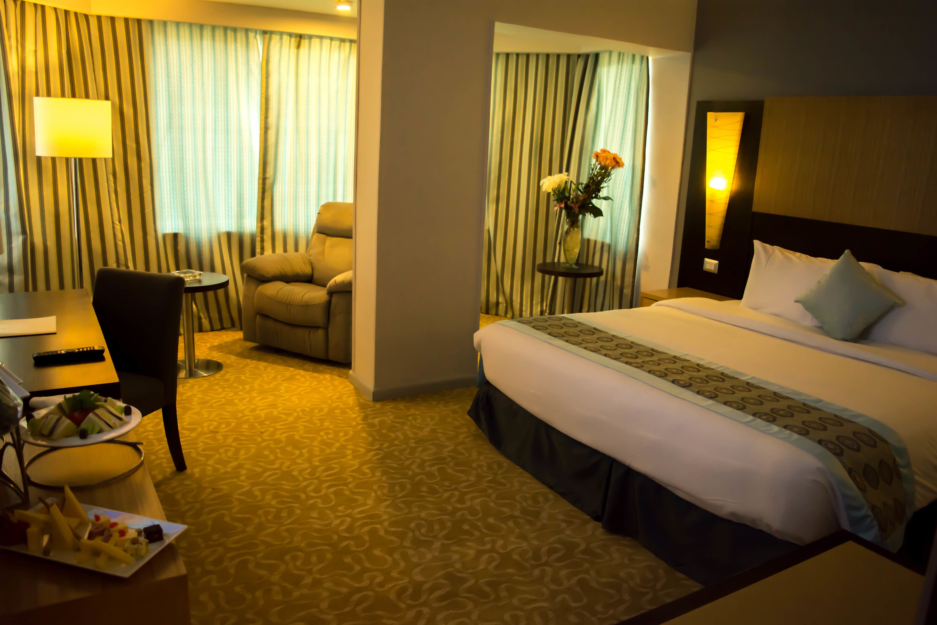 A hotel room with a bed, a chair, a desk, and a small table with a vase of flowers.