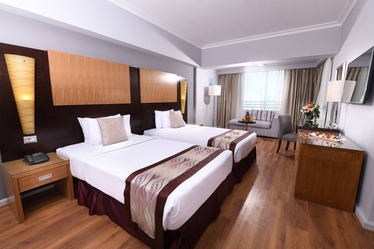 A hotel room with two beds, a desk, a chair, and a mirror.