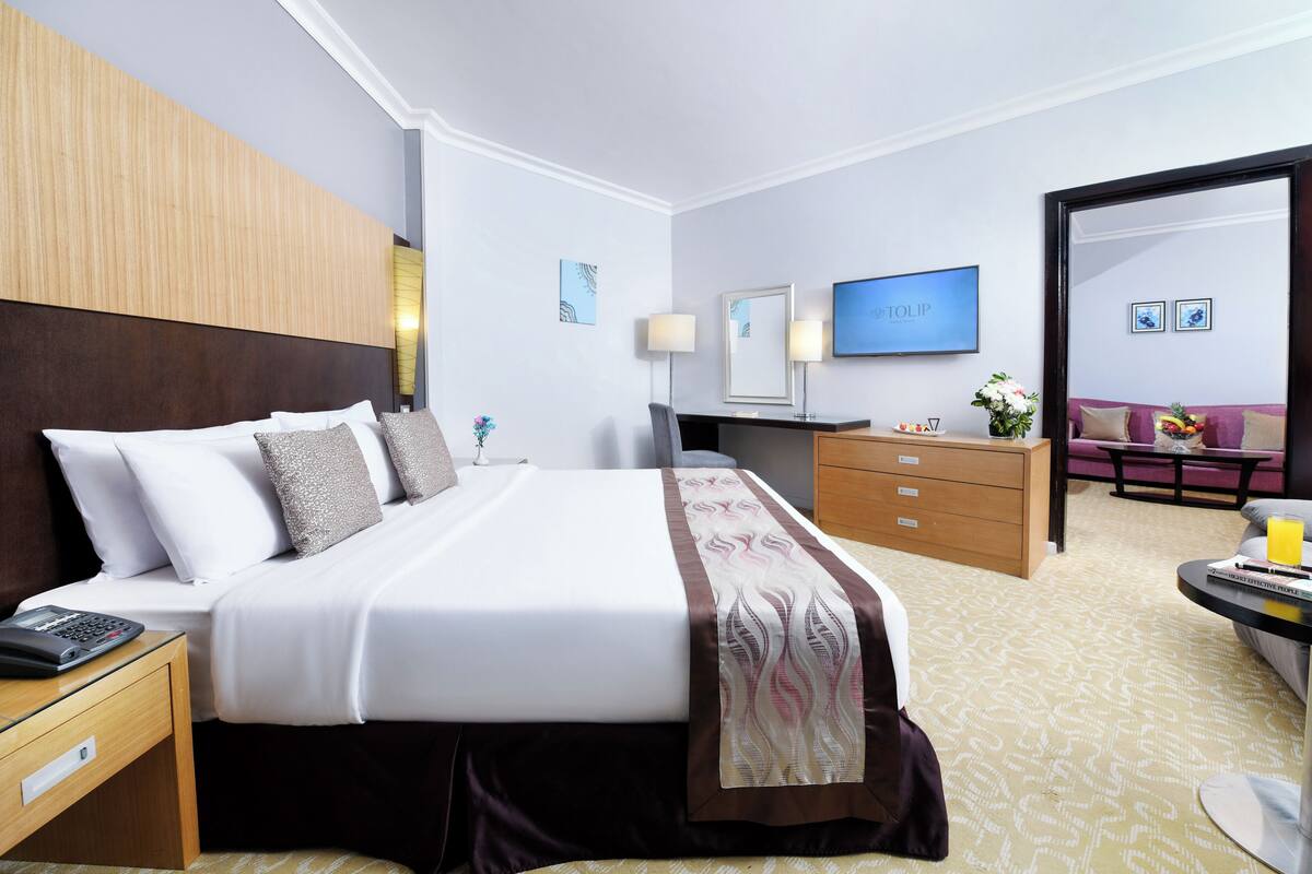 A hotel room with a bed, bedside table, desk, chair, dresser, and a TV on the wall.