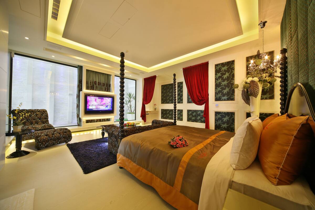 A modern bedroom with a large bed, a TV, a sofa, and a chandelier.