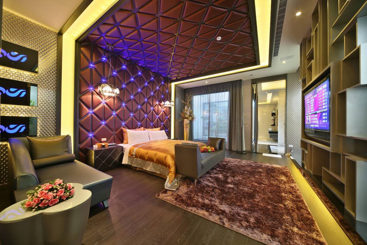 A modern hotel room with a bed, a sofa, a TV, and a decorative wall.