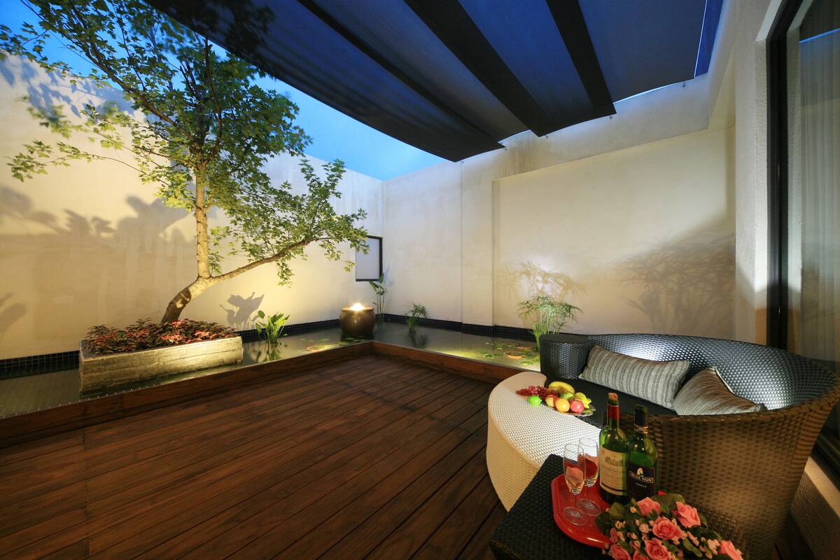 A wooden deck with a seating area, a table with a bottle and glasses, and a potted plant.