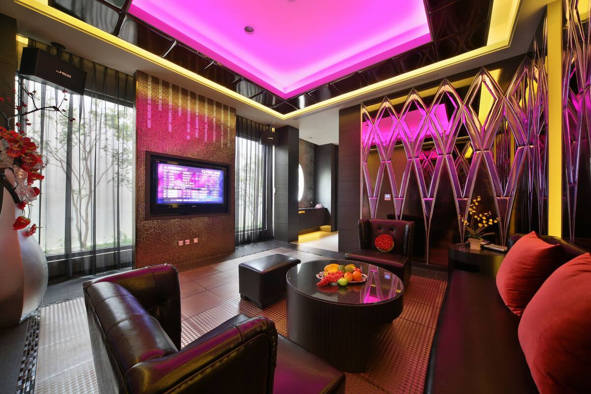 A modern lounge area with leather seating, a round coffee table with fruit, and a flat-screen TV.