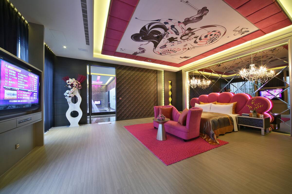 A modern hotel room with a large bed, a pink sofa, a TV, and a decorative ceiling.