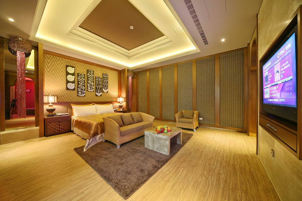 A well-lit hotel room with a large bed, a sofa, a coffee table, and a TV.