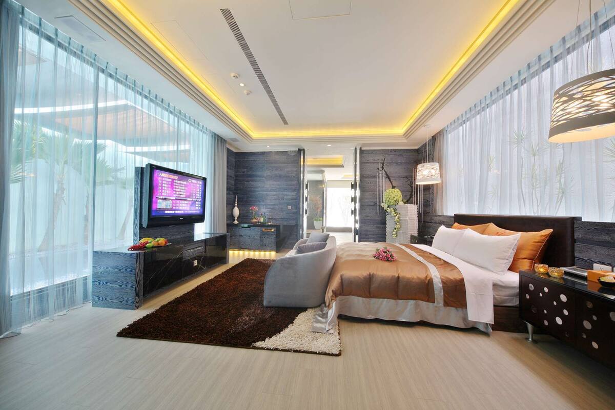 A modern bedroom with a large bed, a TV, and a seating area.