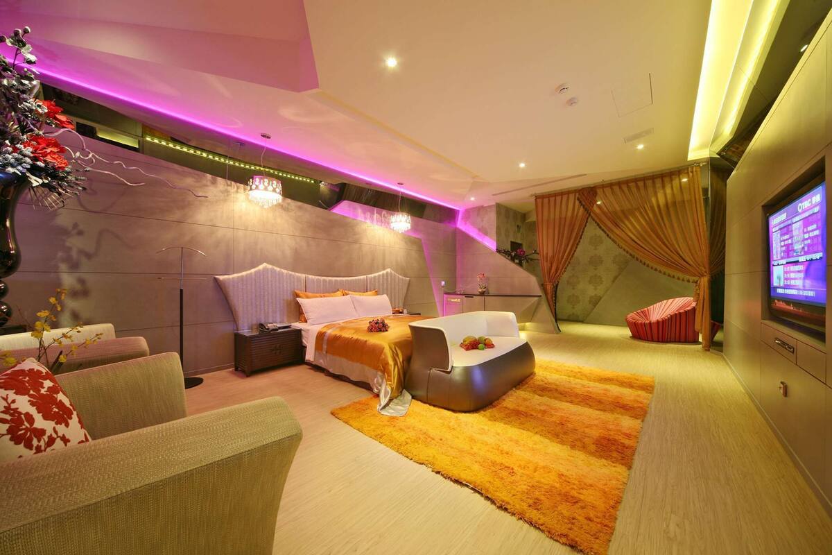 A modern bedroom with a bed, a sofa, a TV, and a unique seating area.