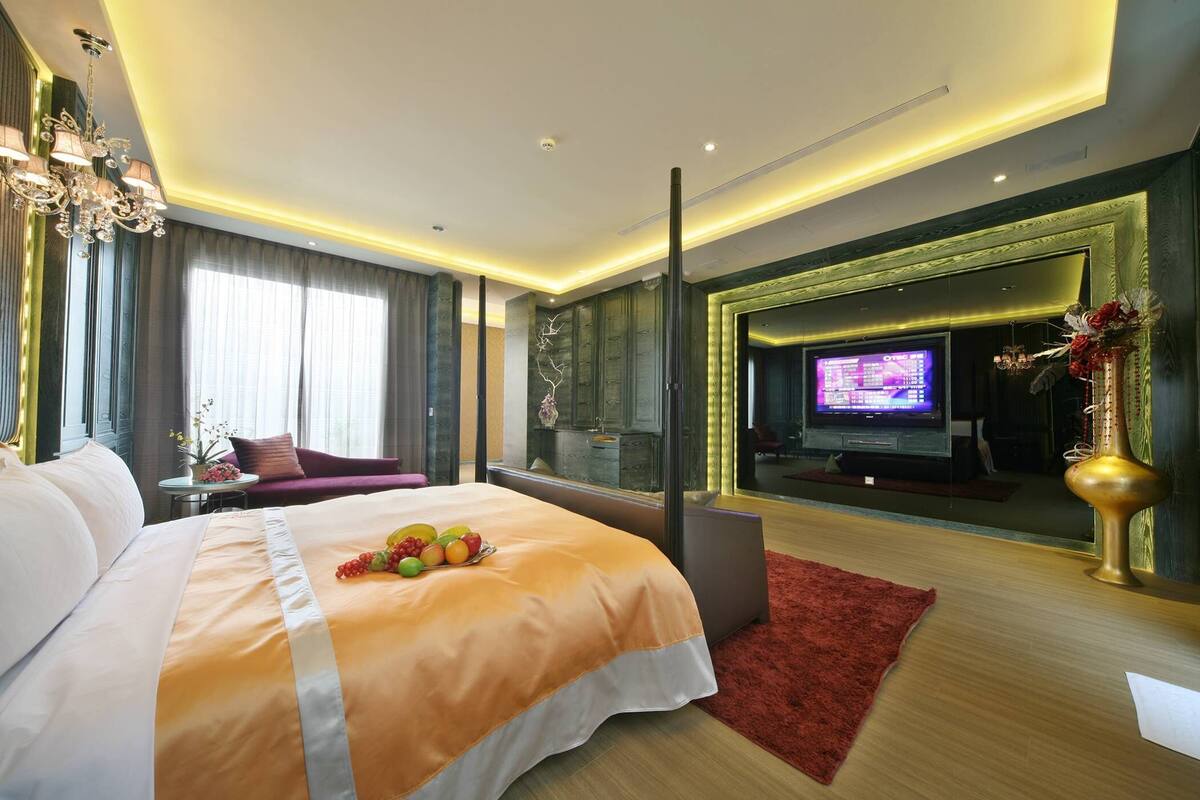 A modern hotel room with a large bed, a TV, and a seating area with a red rug.