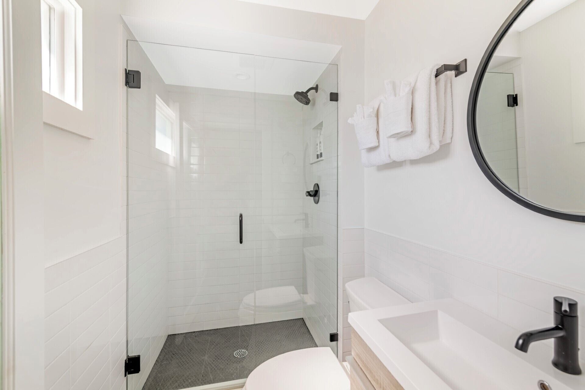 A modern bathroom with a glass-enclosed shower, a white toilet, and a round mirror.