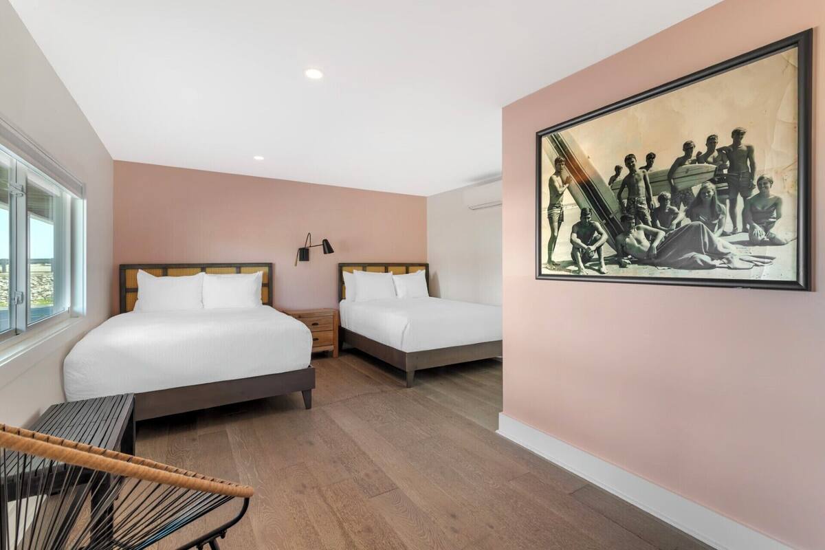 A hotel room with two beds, a chair, a painting, and a window.
