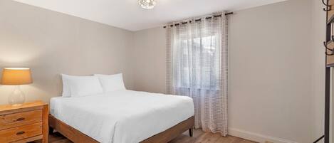 Een slaapkamer met een houten bed, een nachtkastje met een lamp en een raam met gestreepte gordijnen.