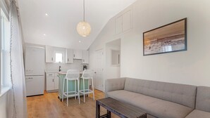 A modern living room with a grey sofa, a wooden coffee table, and a kitchen area with white cabinets and a bar stool. - Ocean Surf at York Beach (York Beach)