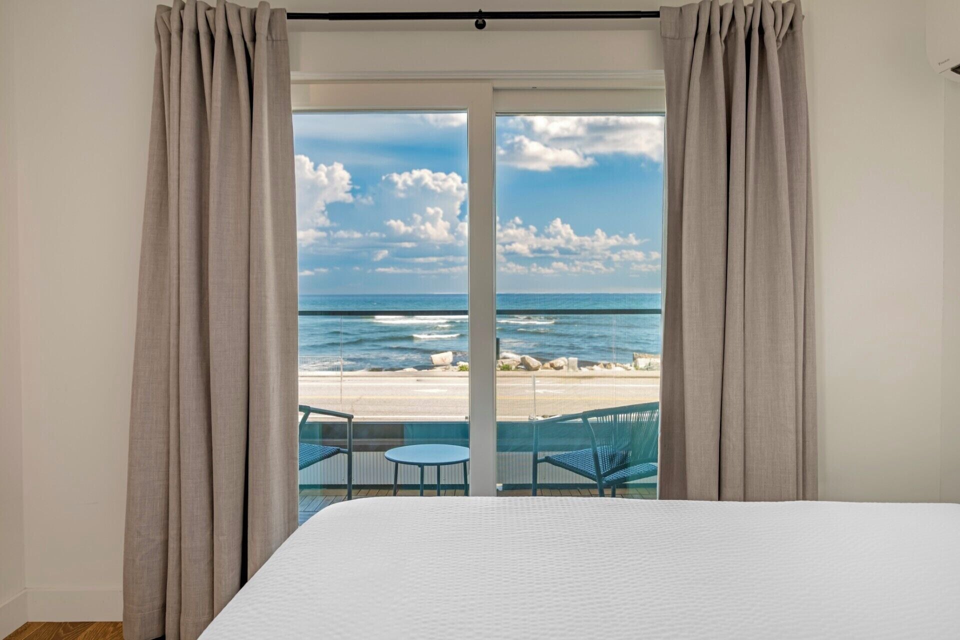 Un dormitorio con una cama grande, vistas a la playa y un balcón con sillas.