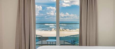 Une chambre avec un grand lit, une vue sur la plage et un balcon équipé de chaises.