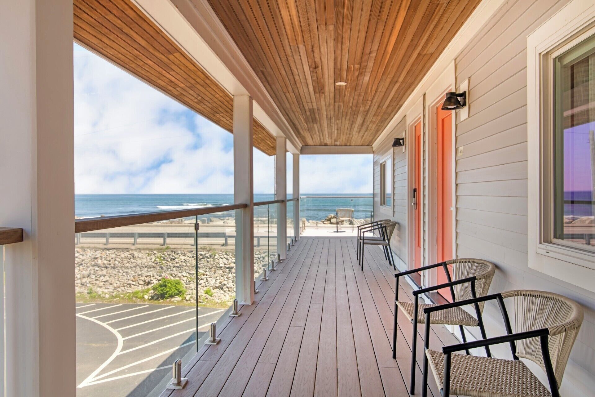 Una terraza de madera con sillas, vista a la playa y barandilla.