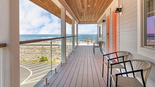 A wooden deck with chairs, a view of the beach, and a railing. - Ocean Surf at York Beach (York Beach)
