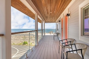 A wooden deck with chairs, a view of the beach, and a railing. - Ocean Surf at York Beach (York Beach)