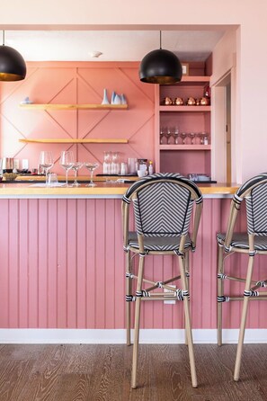 A bar area with two chairs and a counter, pink walls, and shelves with glasses and bottles. - Ocean Surf at York Beach (York Beach)