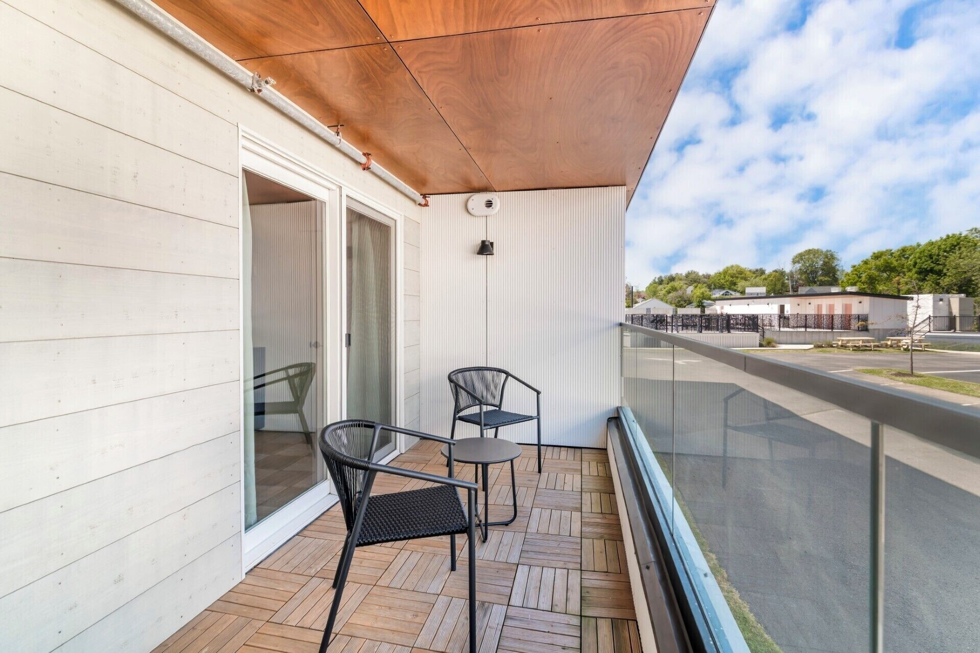 A balcony with two chairs, a table, and a view of a building and trees.