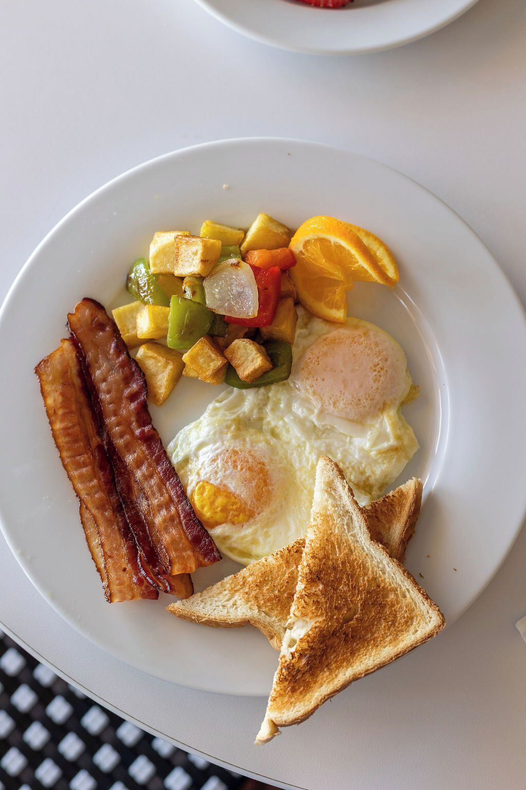 A plate of breakfast food including eggs, bacon, toast, and a fruit salad.