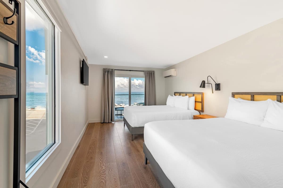 A hotel room with two beds, a TV, a window with a view of the sea, and a balcony.