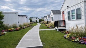 A row of mobile homes with a central pathway, surrounded by well-maintained lawns and flower beds. - Ocean Surf at York Beach (York Beach)
