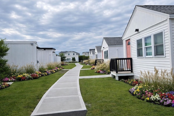A row of mobile homes with a central pathway, surrounded by well-maintained lawns and flower beds. - Ocean Surf at York Beach (York Beach)