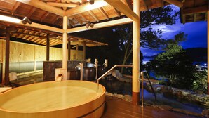 A wooden hot spring bath area with a wooden deck, stone basin, and a view of the outdoors at night. - Todaya (Toba)