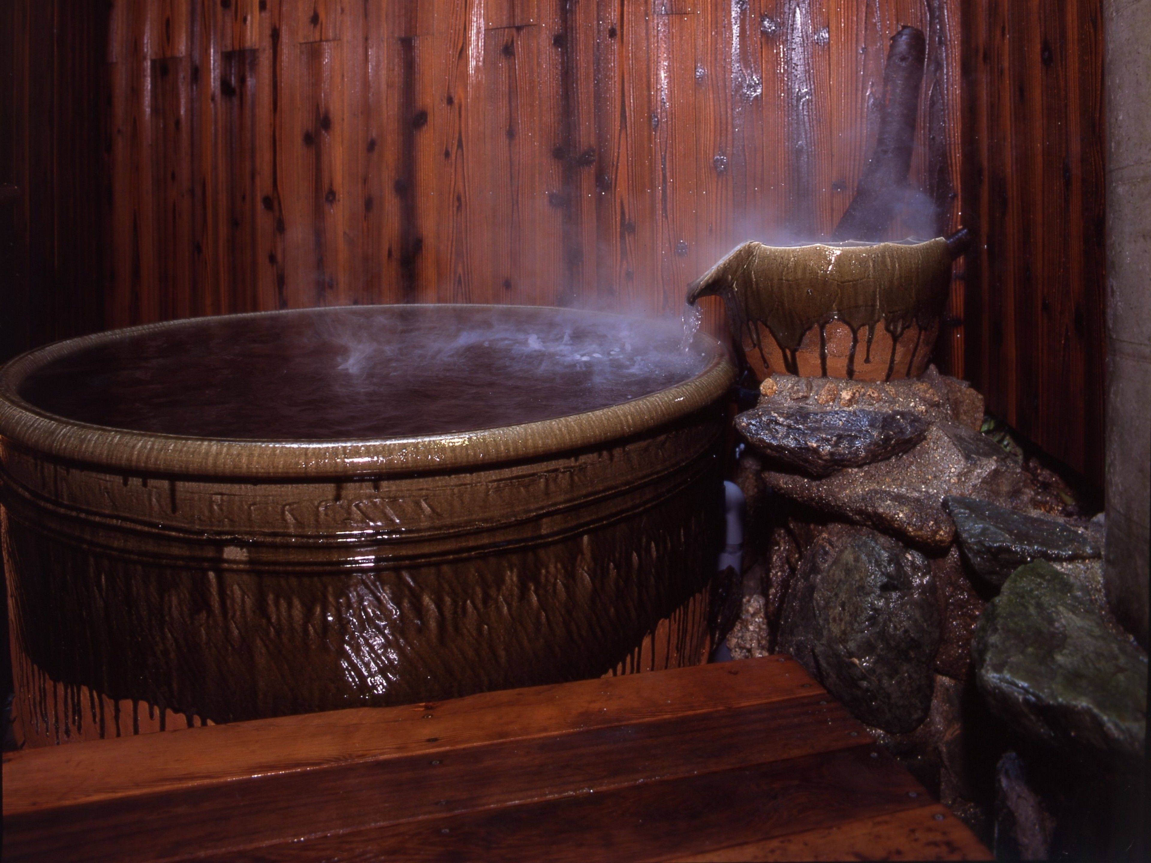 A hot tub with steam rising from it, surrounded by wooden walls and a stone structure.