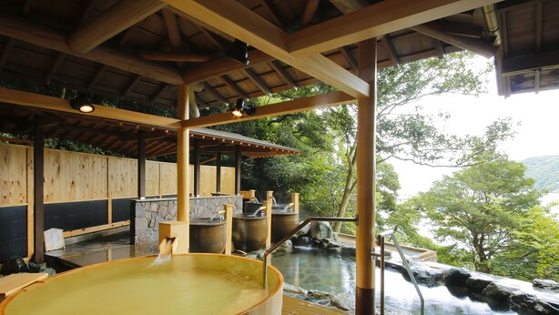 A traditional Japanese onsen with wooden tubs, stone walls, and a view of a natural landscape. - Todaya (Toba)