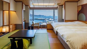 A hotel room with a bed, a desk, a chair, and a view of a harbor with boats. - Todaya (Toba)
