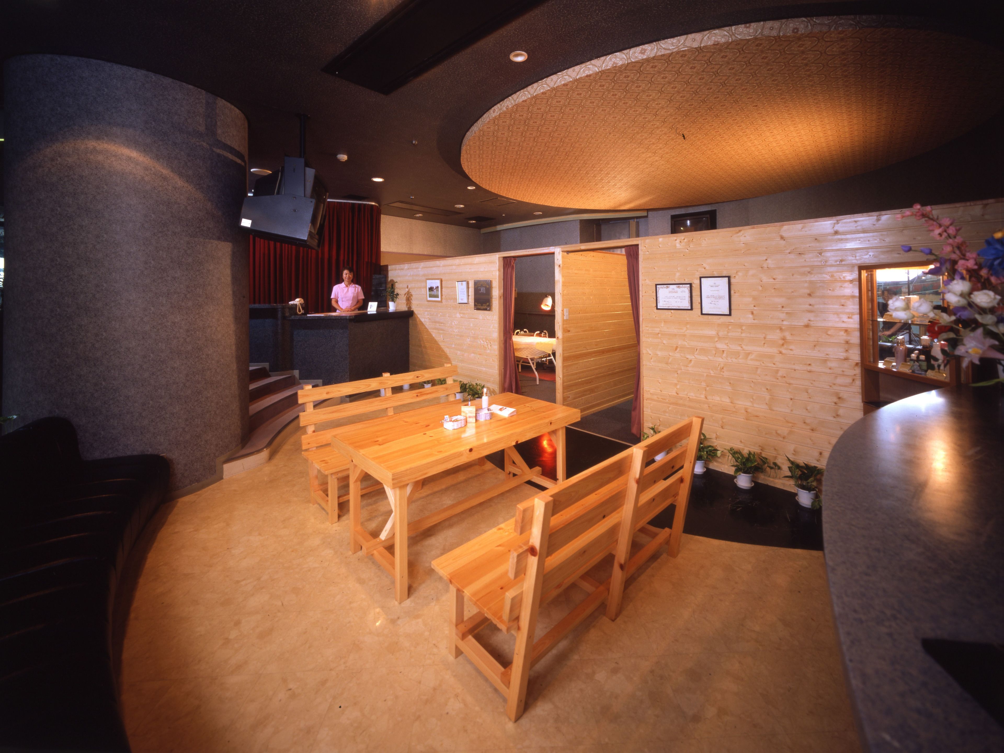 Een restaurant interieur met houten tafels en banken, een toonbank en een podium met gordijnen.