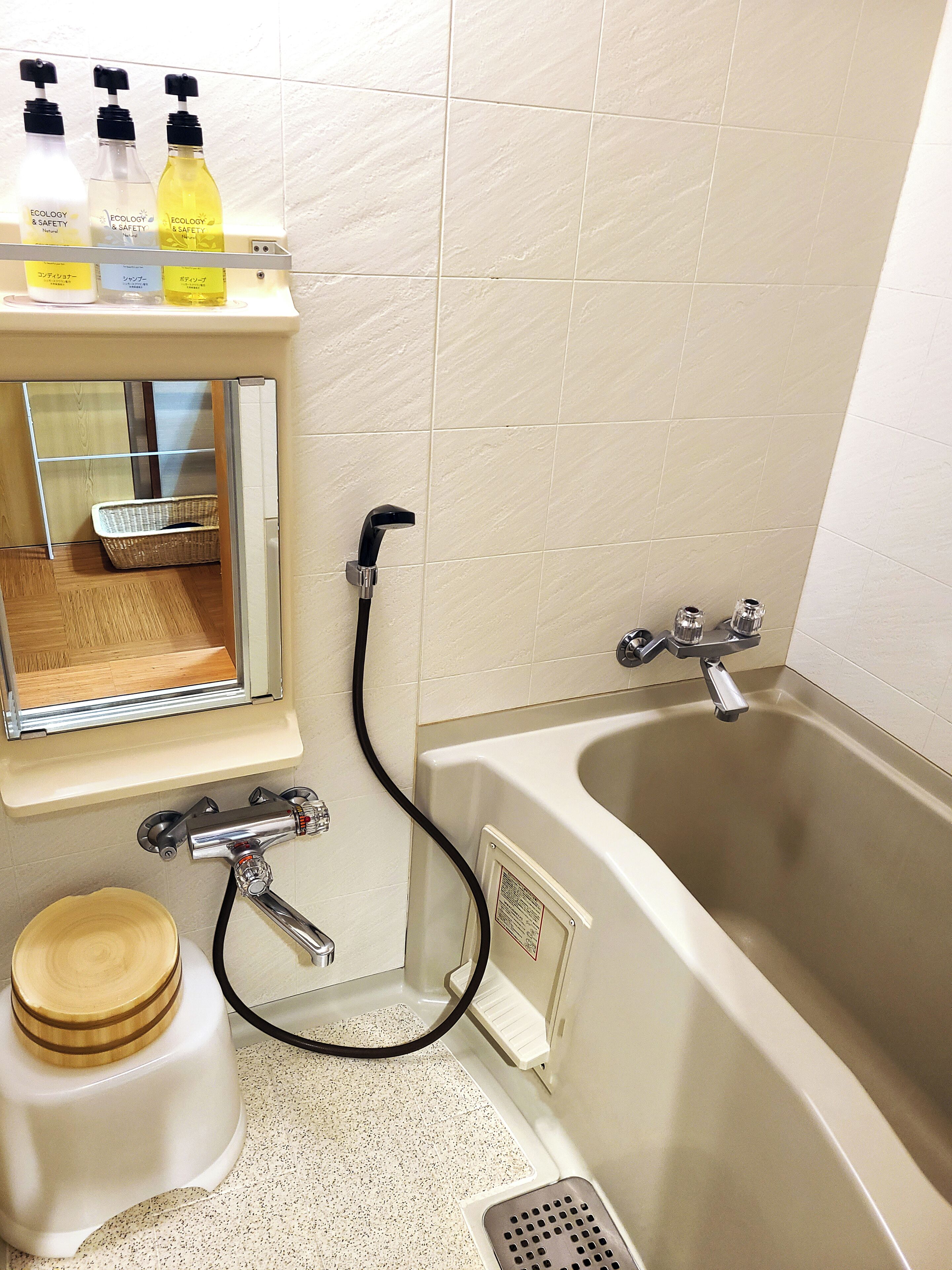 A bathroom with a bathtub, a shower, and a toilet. There are three bottles of toiletries on a shelf.