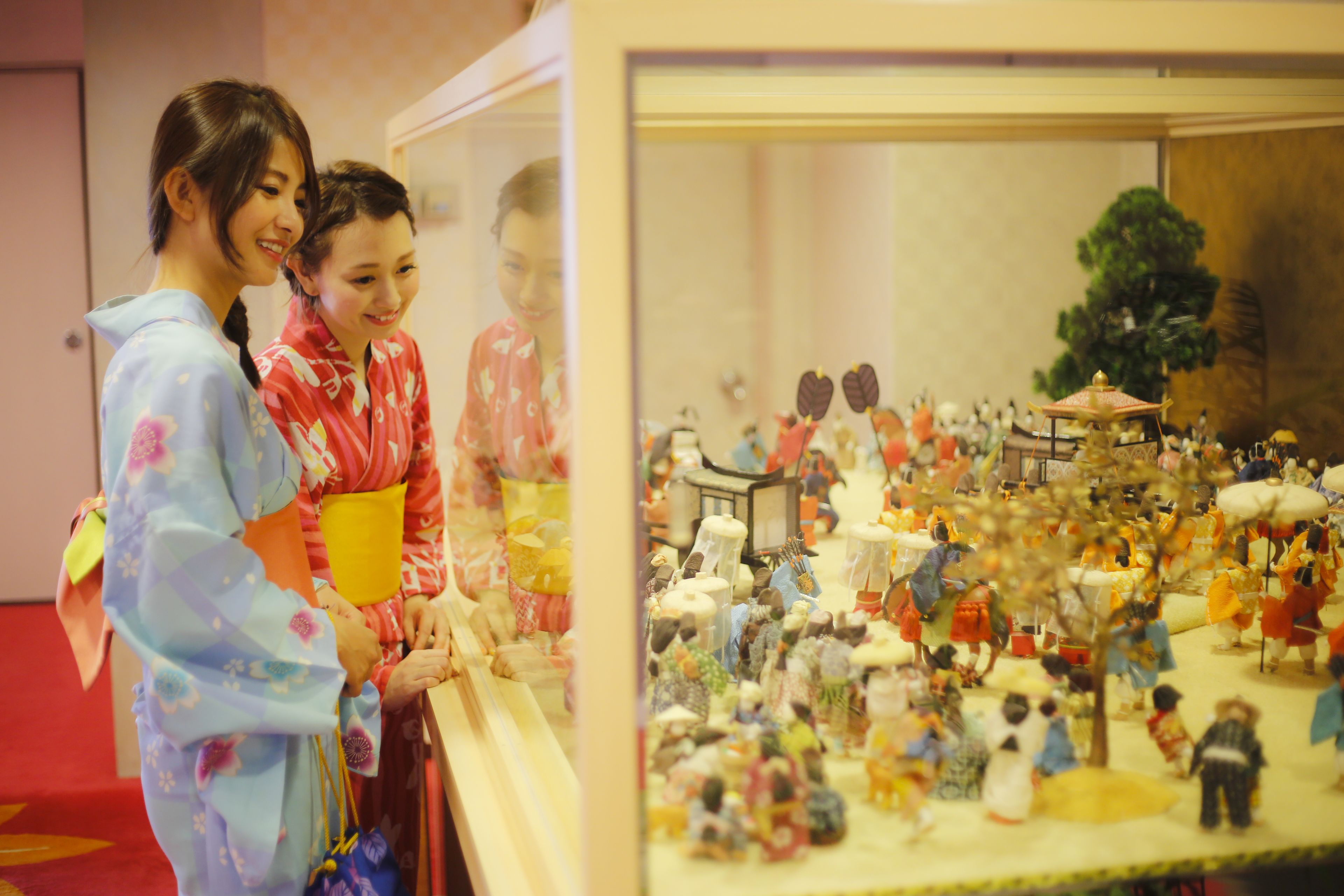 A display of traditional dolls and figures in a glass case, with two people observing.