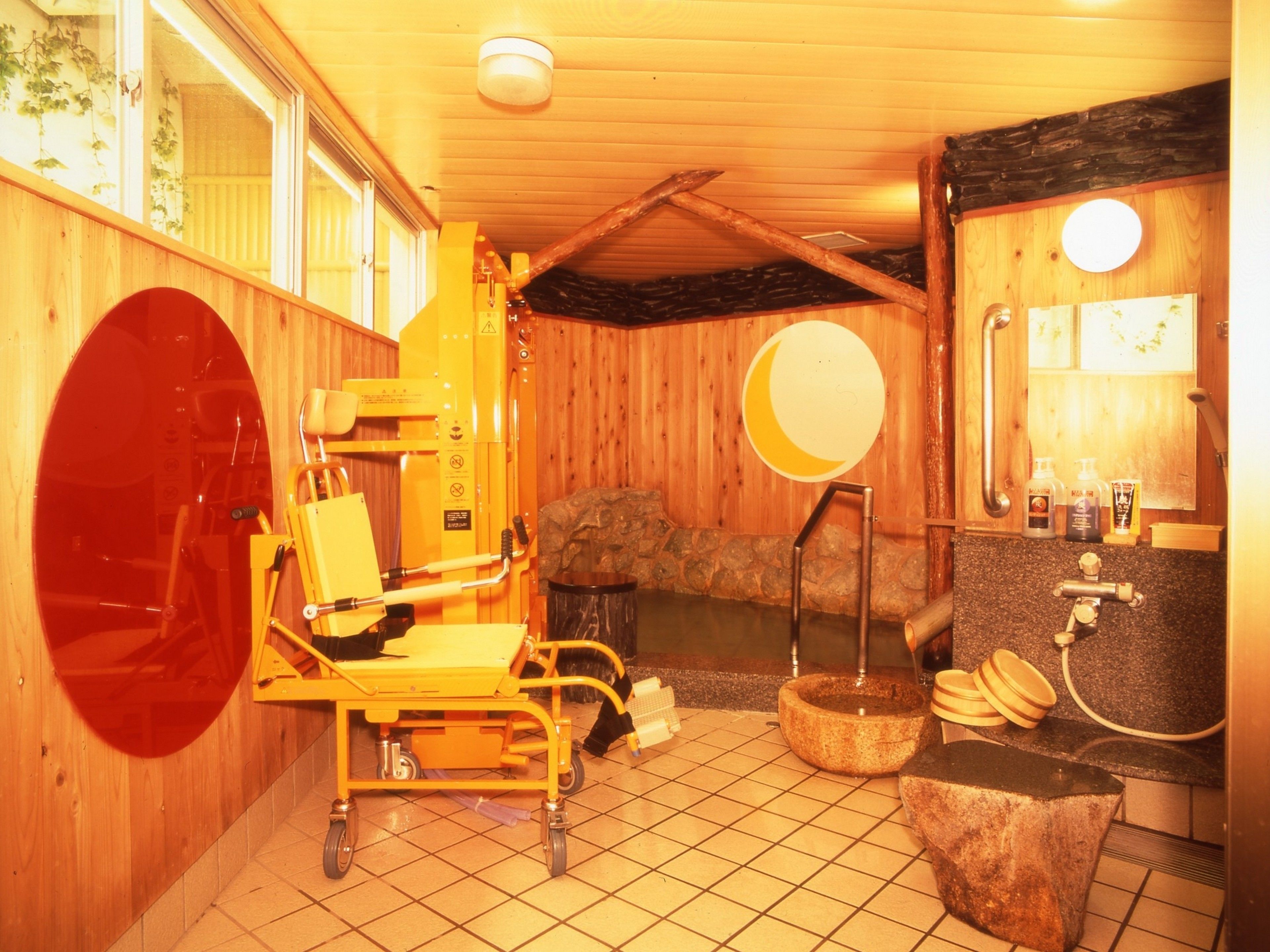 A sauna room with a wooden interior, a massage table, a stone basin, and a mirror.