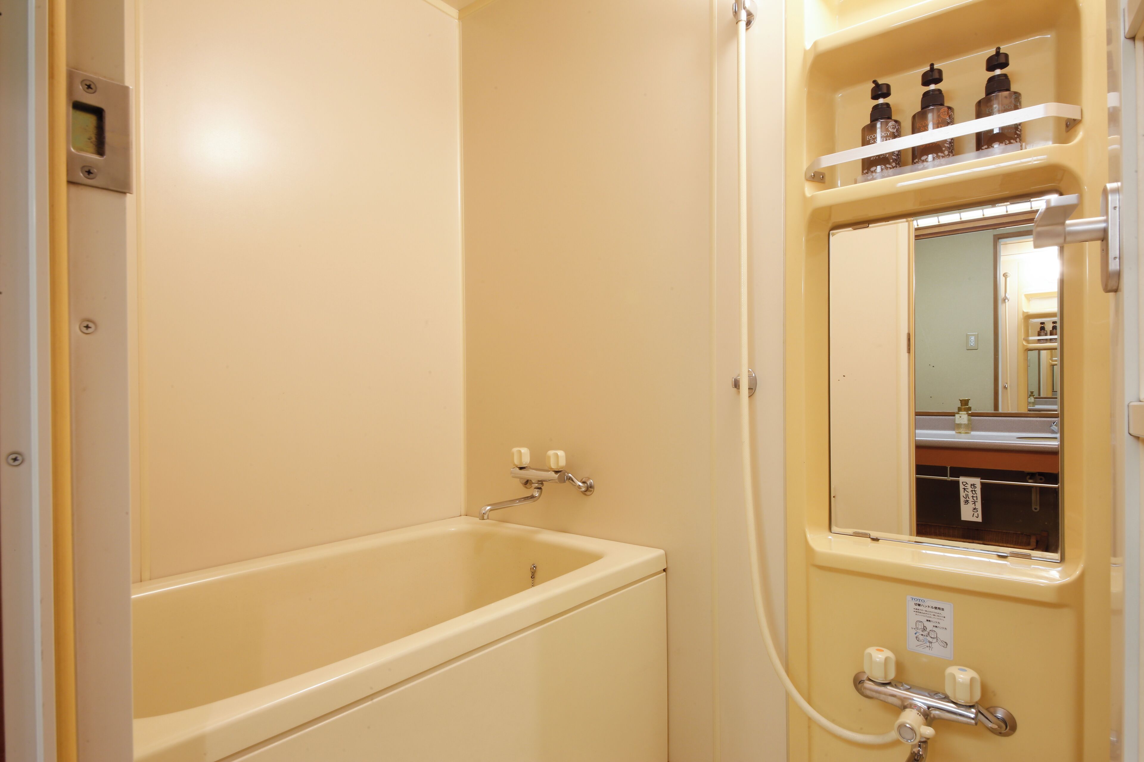 A bathroom with a bathtub, a mirror, and a shelf with bottles.