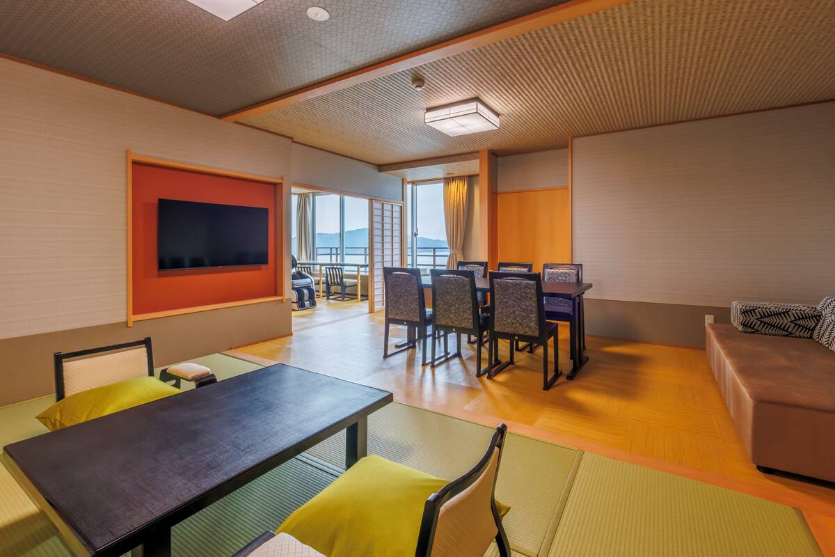 A modern hotel room with a dining area, a sofa, and a TV mounted on the wall.
