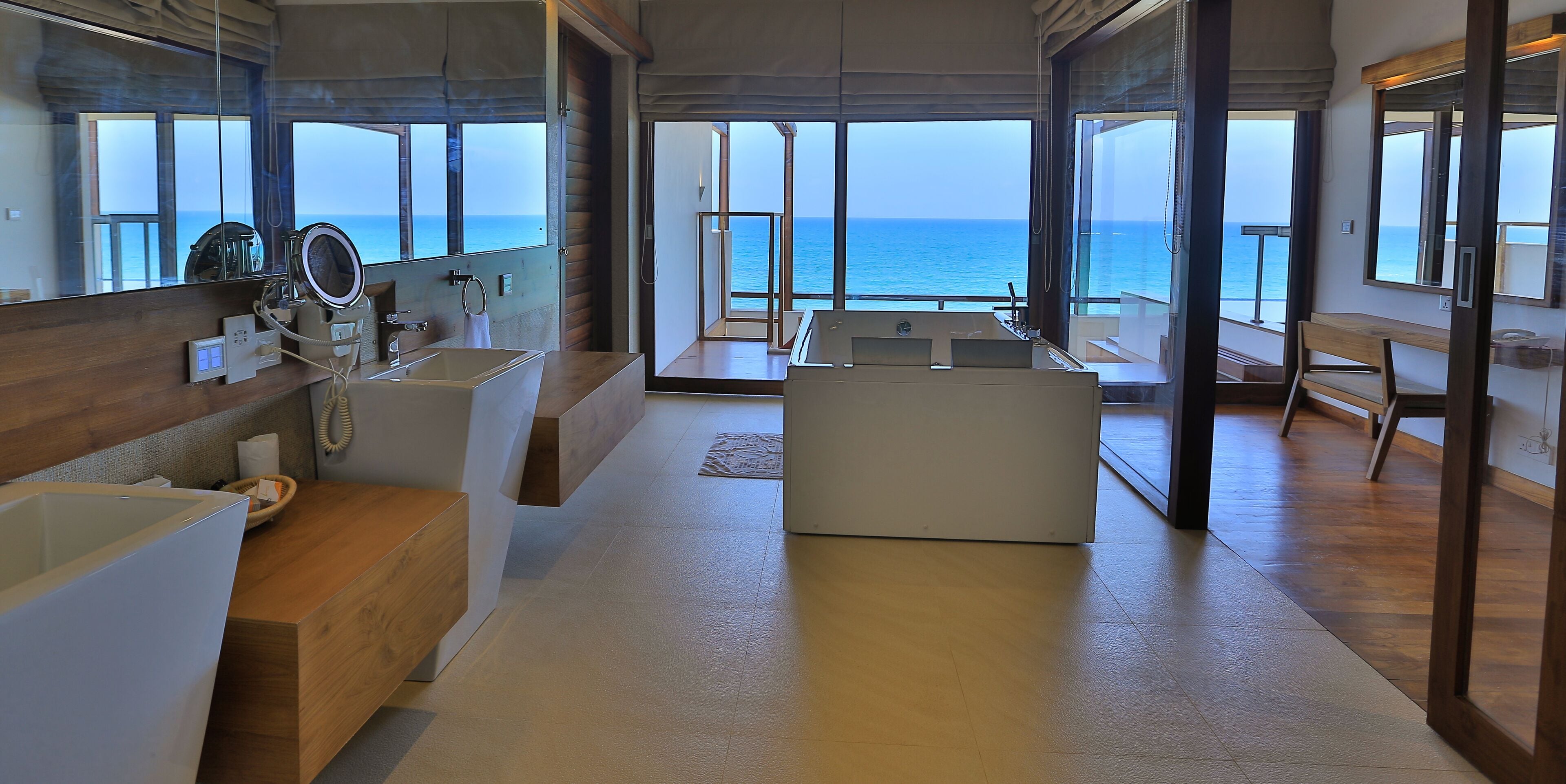 Un baño moderno con una bañera grande, un tocador con espejo y una zona de ducha. La habitación tiene ventanas amplias con vista al océano.