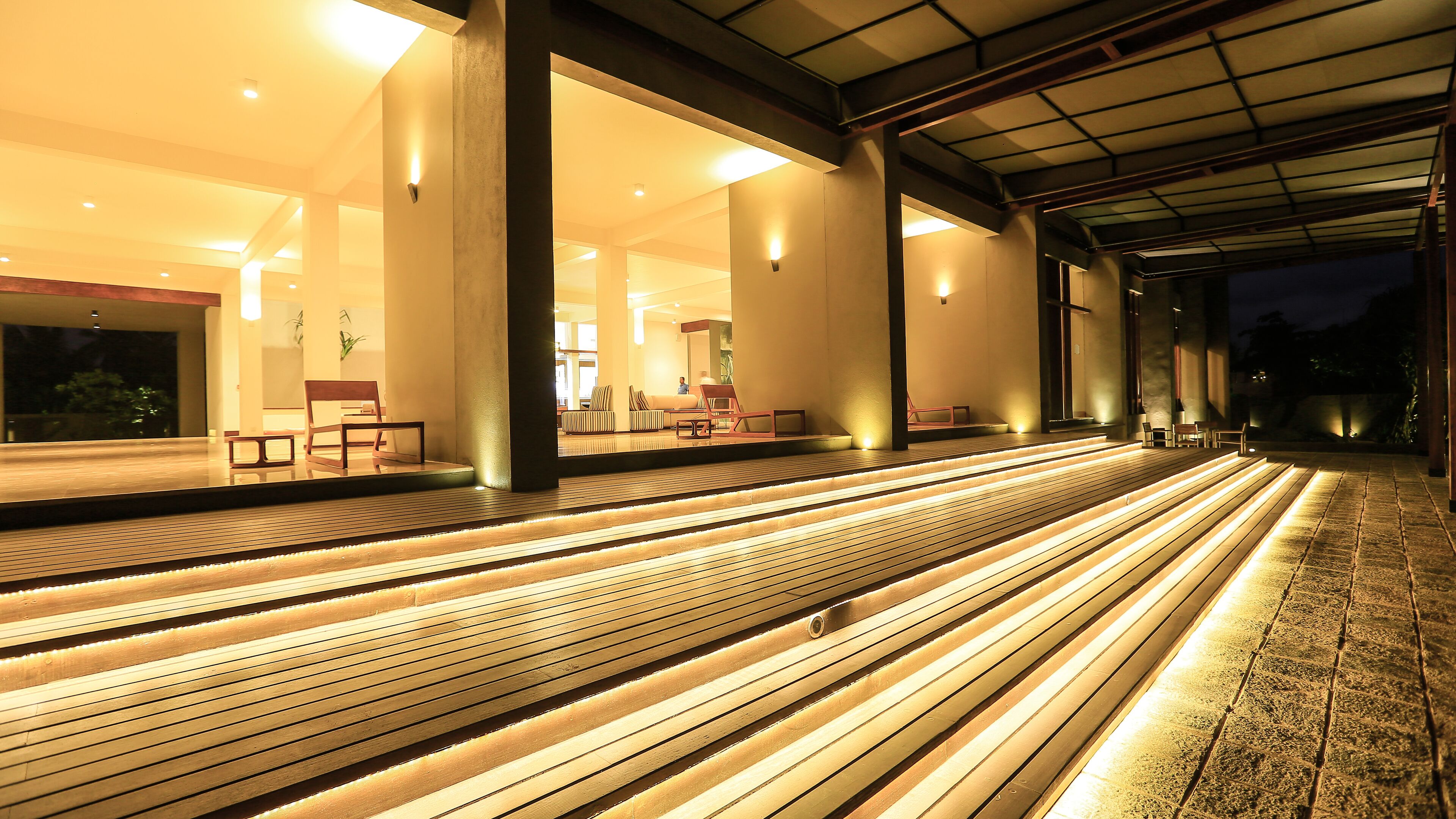 Un espacio exterior bien iluminado con escalones de madera que conducen a una zona de estar, con sillas y mesas.