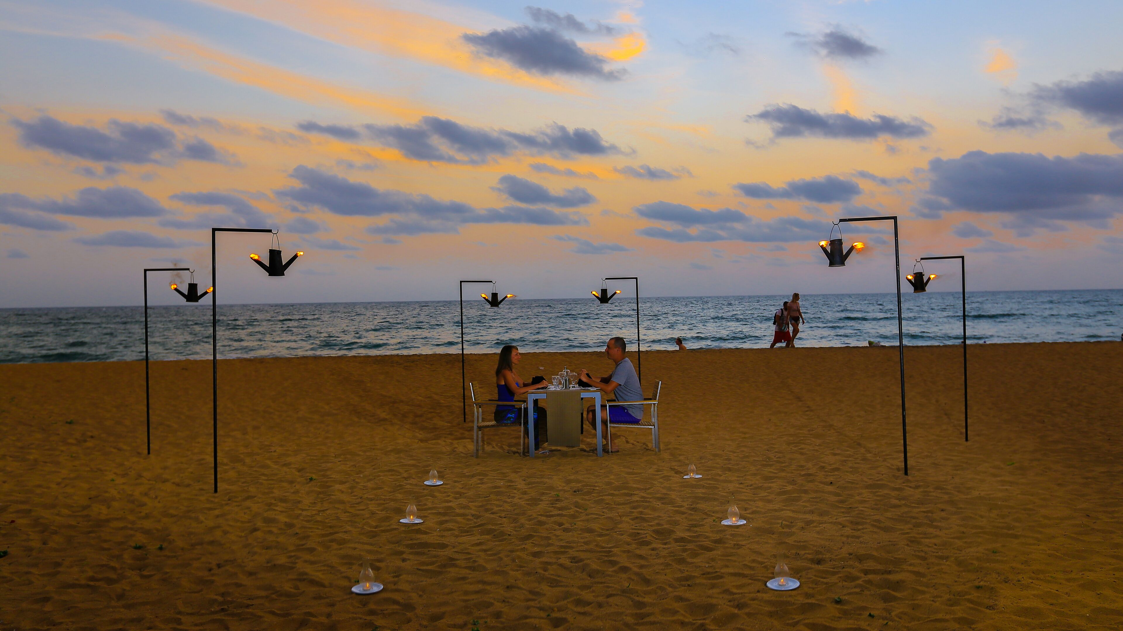 A beachside dining setup with a table and chairs, surrounded by sand and ocean views.