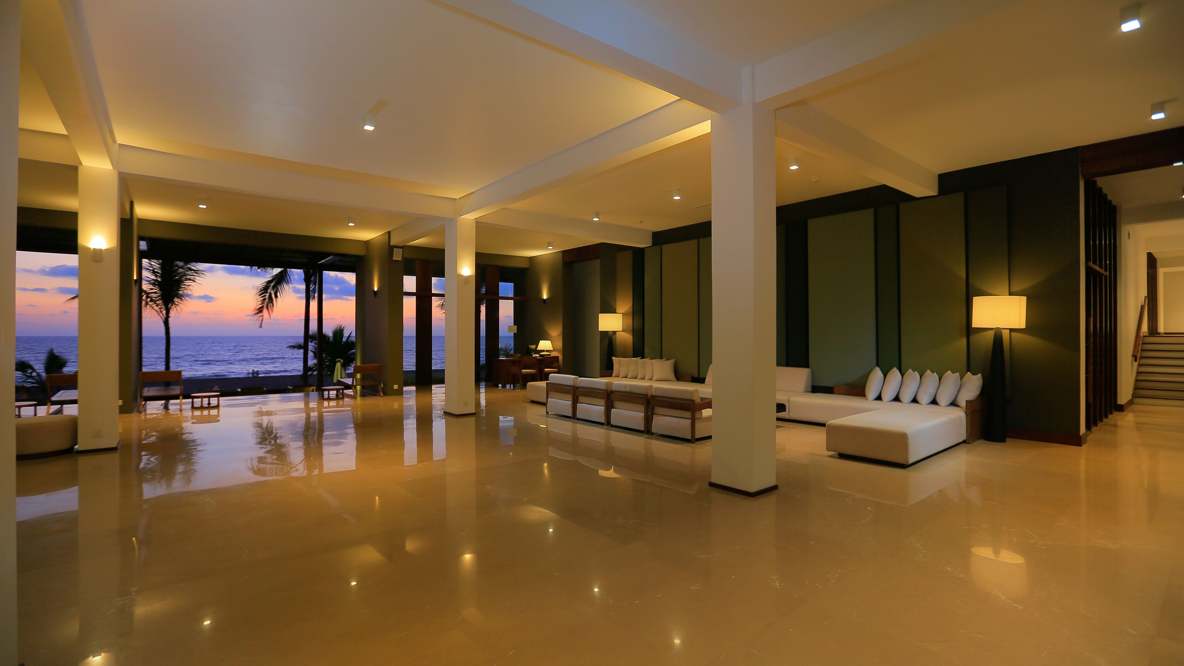 Un vestíbulo amplio y luminoso con vista al océano, una zona de estar con sofá y sillones, y una escalera que conduce a otras áreas.