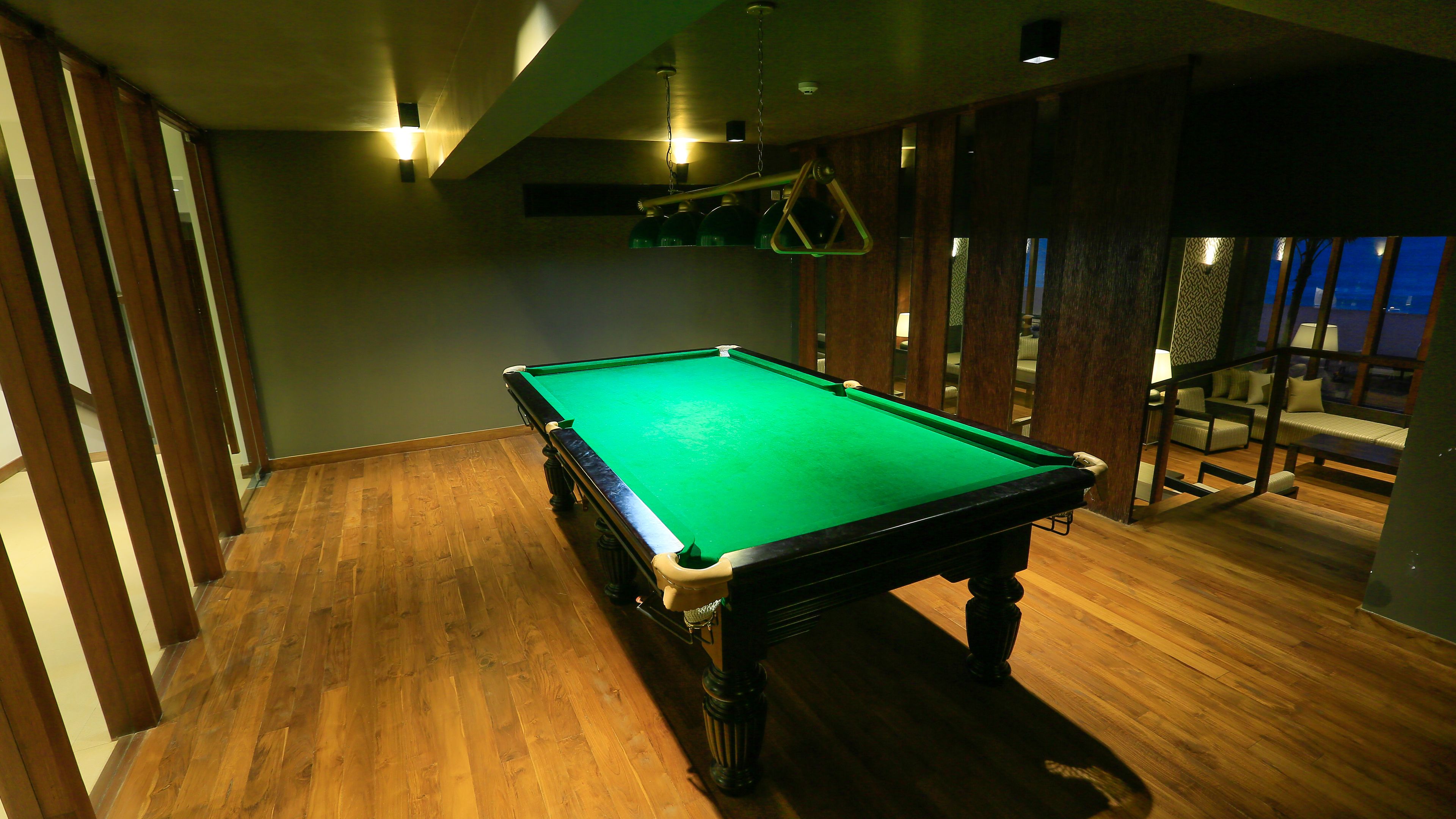 A pool table in a room with wooden flooring and a view of a balcony with seating.