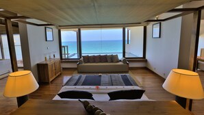A room with a large window overlooking the sea, a sofa, a bed with a rug, and two lamps. - Pandanus Beach Resort & Spa (Induruwa)