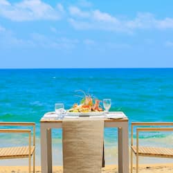 Dine al fresco on the beach with a table set for two, complete with a delicious meal and refreshing drinks.